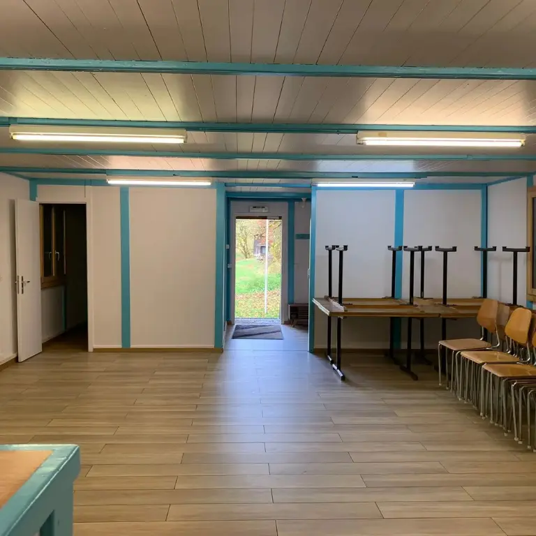 Salle à manger du chalet scout avec 8 tables et 30 chaises, vue depuis la cuisine