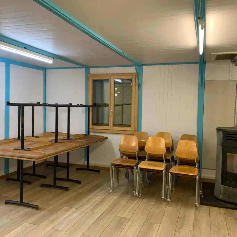 Salle à manger du chalet scout avec 8 tables et 30 chaises, vue depuis la cuisine